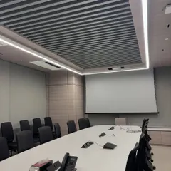 This is the conference room before the presentation begins. The motorized 120-inch tab-tensioned ALR screen is retracted, maintaining the room's clean aesthetic. The setup includes integrated conference phones for a complete meeting solution.