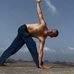 Holding Trikonasana, or Triangle Pose, by the sea. This is a fundamental standing pose that stretches the hamstrings, hips, and spine, creating length along the sides of the body.