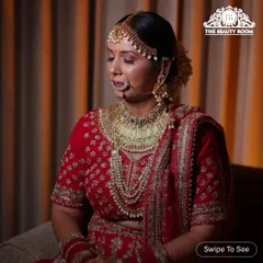 A serene moment captured before the ceremony. This classic bridal makeup features soft, shimmering eyes and a bold red lip, perfectly matching her traditional red lehenga and heavy gold jewellery.