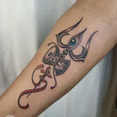 A unique composition featuring the Trishul, Damru, and the third eye, combined with the Om symbol. The red accents create a striking contrast and add a layer of energy to this spiritual forearm tattoo.