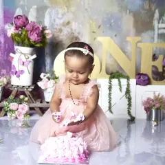 A classic first birthday cake smash moment. Dressed in a beautiful pink gown, this little one is enjoying her very first taste of birthday cake in a lovely floral garden setting.