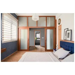 This bedroom design is all about clean lines and clever use of space. A wall of sliding doors, framed in wood with frosted glass panels, conceals a spacious walk-in wardrobe. This solution keeps the room feeling uncluttered and serene while providing ample storage, blending functionality with a calm, modern aesthetic.