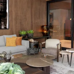 A living room corner where every object is chosen to speak without speaking. The grain of the custom veneer, the texture of the cushions, and the collected shells and sculptures all contribute to a layered, warm, and soulful environment.