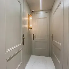 Details matter, even in the passages. This hallway in a luxurious private residence features classic paneled doors and walls, complemented by elegant brass handles and a vintage-style wall sconce.