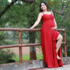 A solo portrait during an outdoor maternity shoot. The vibrant red gown stands out beautifully against the natural backdrop, creating a powerful and serene image of the mother-to-be.