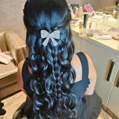 A playful and chic half-up style featuring a combination of braids and curls, accented with a sparkling bow clip. This is a great party hairstyle for younger clients.