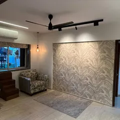 This living room features a subtle leaf-patterned wallpaper accent wall, creating a calm and natural focal point. The space is lit with modern track lighting and a hanging industrial-style bulb.