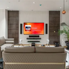 A view of a complete living room entertainment system we installed. It features a large screen flanked by tower speakers, multiple soundbars, and Devialet Phantom speakers, all integrated to work together for music, movies, and more.
