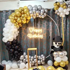 A chic black, white, gold, and silver balloon ring backdrop for a birthday party, complete with a cute panda detail and a bright neon sign.