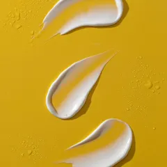 A macro shot of three perfect skincare cream smears on a bright yellow background. The lighting highlights the glossy texture and subtle shadows, creating a visually satisfying image that speaks to the product's quality.