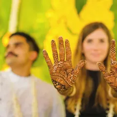 The intricate beauty of Mehendi is a key part of the celebration. Here, a guest proudly shows off her detailed henna design against a backdrop of bright yellow marigolds.