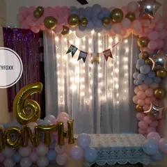 A sweet 6-month celebration setup at home, with a backdrop of fairy lights, a pink and blue balloon arch, and foil balloons marking the milestone.