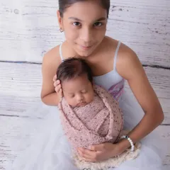 A proud big sister holds her swaddled baby brother. I guide older siblings to hold the baby safely and comfortably, resulting in a portrait that is both beautiful and secure.