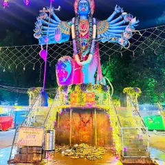 A massive deity statue at Amma Shakthi Peeta, illuminated with vibrant pink and blue lights for a dramatic nighttime effect.