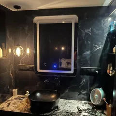 A closer look at the vanity area in a black-themed bathroom. The LED mirror provides excellent task lighting, while the open shelving and countertop offer space for daily essentials.