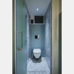 A modern bathroom design with terrazzo-style tiles and a fluted accent wall in a calming blue-green hue. The wall-mounted toilet and frosted glass door help to maximize the sense of space.