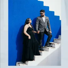 A bold and stylish pre-wedding portrait. The contrast of the vibrant blue wall, the white stairs, and the couple's black outfits creates a modern, high-fashion look that is both artistic and memorable.