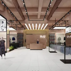 A front-facing view of the apparel store's reception desk, showing the cohesive design language. The industrial ceiling with exposed ducts and track lighting contrasts with the warm, lime-plastered walls and minimalist branding.