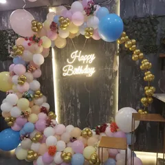 A closer look at a pastel-themed birthday balloon arch. This circular arrangement combines soft pink, blue, and yellow balloons with pops of gold chrome and small floral details for an elegant finish.