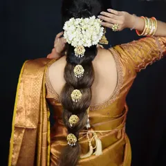 A classic South Indian bridal braid, also known as 'Jada'. It is decorated with traditional gold ornaments called 'billai' and fresh jasmine flowers for a timeless look.