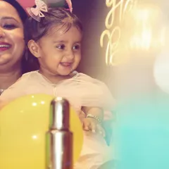 A close-up candid shot of the birthday girl smiling, with a 'Happy Birthday' sign glowing in the background. The soft lighting and genuine smile make this a precious memory.
