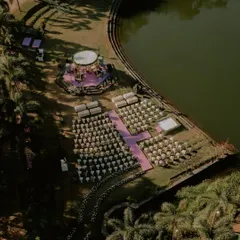 An aerial view of the magnificent lotus-pink mandap set against the serene lake. This shot captures the scale of the setup and the beautiful contrast between the vibrant decor and the natural landscape.