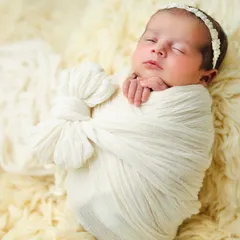 Simplicity at its finest. A newborn is elegantly wrapped in a textured white swaddle with a bow detail, resting on a soft, cream-colored fur blanket for a serene and angelic look.