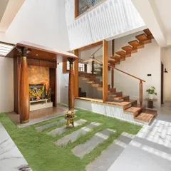 A view of the second courtyard, which houses the pooja mandapam. The design combines traditional wooden pillars with a modern floating staircase and a grass floor, blending cultural heritage with contemporary architecture.