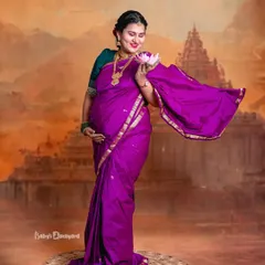 A portrait of pure grace. The mom-to-be glows in a vibrant purple silk saree against a painted temple backdrop, holding a lotus flower to signify purity and beauty.