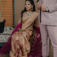 A portrait of the bride, Karishma, seated elegantly in her golden silk saree, giving a glimpse of the complete traditional Maharashtrian bridal look.