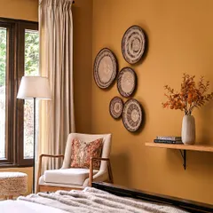 This cozy corner in a bedroom from my Modern Spanish project shows how I use color and texture to create warmth. The mustard-colored wall, woven wall decor, and soft textiles come together to create a calm and inviting reading nook.