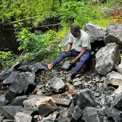 An artisan carefully shaping and splitting locally sourced stone. We prioritize using natural materials found on or near the site to ensure our designs are sustainable and rooted in their environment.
