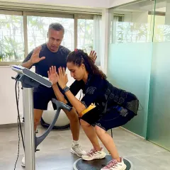 Namrata performs a squat on a BOSU ball while wearing an EMS suit, with Samir guiding her form. This combination is an ultimate challenge for balance, stability, and deep muscle activation.