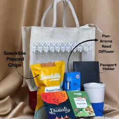 This hamper is a perfect example of practical and sustainable gifting. It includes a reusable jute bag with a lace window, filled with snacks, an eco-friendly mug, a passport holder, a reed diffuser, and a Diwali card.