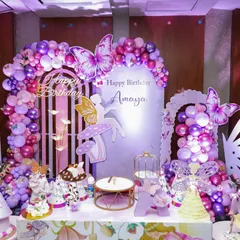 We created a magical butterfly garden for Amaya's birthday. The setup features a stunning backdrop with purple and pink balloon arches, illuminated butterfly wings, and fairy cutouts, making for a truly enchanting photo opportunity.