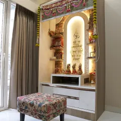 A serene and beautifully designed pooja mandir, with intricate details, warm backlighting, and a comfortable floral stool for daily prayers.