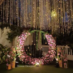 A stunning nighttime view of the circular floral arch I created for an engagement. The pink flowers are beautifully illuminated, and the curtain of fairy lights behind creates a truly magical and romantic ambiance.