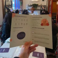 A participant holds up our informational pamphlet from a kombucha workshop. It details what goes into the brew, the benefits, and a guide on how to make your own SCOBY at home.