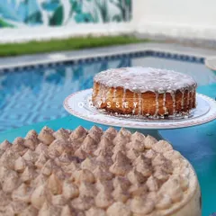 Sweetness by the poolside. This image features a classic glazed cake and a tiramisu, part of our array of desserts crafted to be the delicious conclusion to any fiesta.