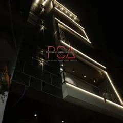 An upward-angle shot of 'The Cursive Abode' facade at night. The linear lighting traces the architectural frames, creating a sense of depth and luxury while accentuating the building's verticality.