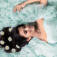 A beautiful overhead shot capturing a moment of pure bliss. The mom-to-be lies on a bed of soft blue tulle, with delicate flowers in her hair, creating an artistic and ethereal portrait.