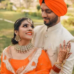 A classic pre-wedding portrait of a Punjabi couple. The bride's upward glance and the groom's loving look create a beautiful connection, highlighting their vibrant orange outfits.
