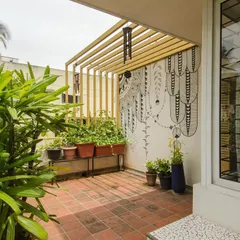 A black and white graphic mural provides a striking contrast to the vibrant plants on this terrace. A simple metal pergola adds structure and defines the space, creating a cozy and artistic outdoor nook.