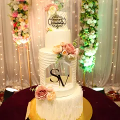 A grand four-tier engagement cake designed to make a statement. It features different textures on each layer, including clean lines, ruffles, and a custom monogrammed window, all brought together with beautiful pastel flowers.