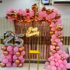 A beautiful 25th anniversary setup featuring a rose gold fringe curtain and a pink and metallic balloon arch. The large silver foil "25" balloons clearly mark the milestone, making it perfect for photos.