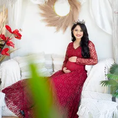 A lovely portrait of a mom-to-be in a red lace gown, seated on our boho studio couch. The soft lighting and gentle pose create a warm and inviting image.