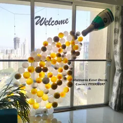 This is a creative and fun decoration for a welcome party. I used balloons to create the effect of champagne pouring out of a bottle against a large window, making for a unique photo spot.