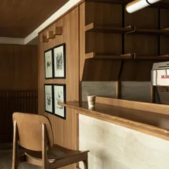 A detail of the coffee bar, where a single stool invites a moment of interaction with the barista. The material palette is restrained and tactile.