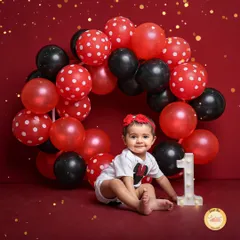 A Minnie Mouse inspired first birthday shoot. The bold red backdrop, polka-dot balloons, and a light-up number '1' create a classic and cheerful setting for this milestone.