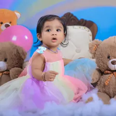 A close-up shot capturing the birthday girl's curious expression. The soft pastel colors of her dress perfectly match the rainbow theme.